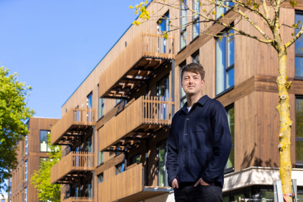 Timo Broersen poseert voor houten appartementencomplex in aanbouw